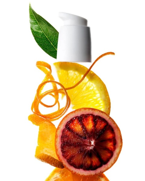 A high-end product photography shot featuring a skin serum pump bottle floating amidst fresh sliced blood orange and citrus zest.